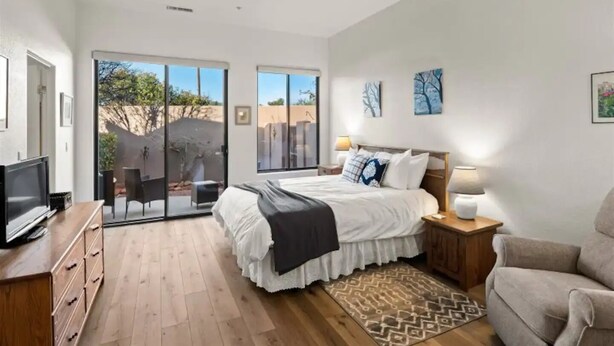 A modern bedroom with a large bed, a TV, a desk, and a sliding glass door leading to an outdoor area. - Golf & Pickleball at Casa de Cielos (Sedona)