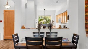A dining area with a wooden table and chairs, a hanging light fixture, and a window with a view of greenery. - Golf & Pickleball at Casa de Cielos (Sedona)