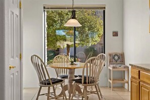 Un comedor con una mesa redonda y cuatro sillas, una lámpara colgante y vistas al exterior con vegetación.