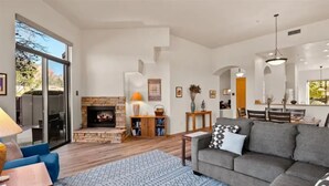 A spacious living room with a fireplace, a dining area, and a large window. - Golf & Pickleball at Casa de Cielos (Sedona)