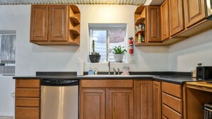 Una cocina con armarios de madera, lavavajillas de acero inoxidable, una ventana con plantas y un extintor.