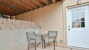 Un patio con pared de ladrillo, una puerta blanca y dos sillas de mimbre alrededor de una mesita.