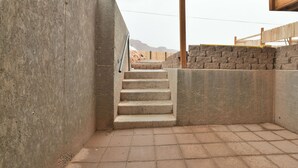 Una escalera de concreto lleva a una terraza de madera, rodeada de muros de piedra y un piso de ladrillo.