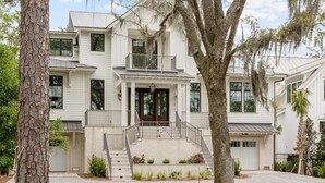 Une maison à deux étages avec un porche à l’avant, un escalier et un grand arbre dans le jardin.