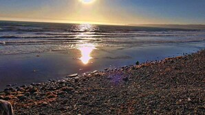 Een strand met kiezels en golven, badend in fel zonlicht.