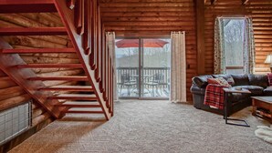 L’intérieur d’une cabane en rondins, avec un escalier, un canapé en cuir noir, une petite table et, à travers une porte vitrée, une vue sur un patio extérieur.