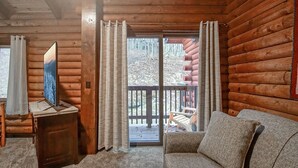 L’intérieur d’une cabane en rondins, avec un canapé, un meuble en bois et une grande fenêtre avec des rideaux.