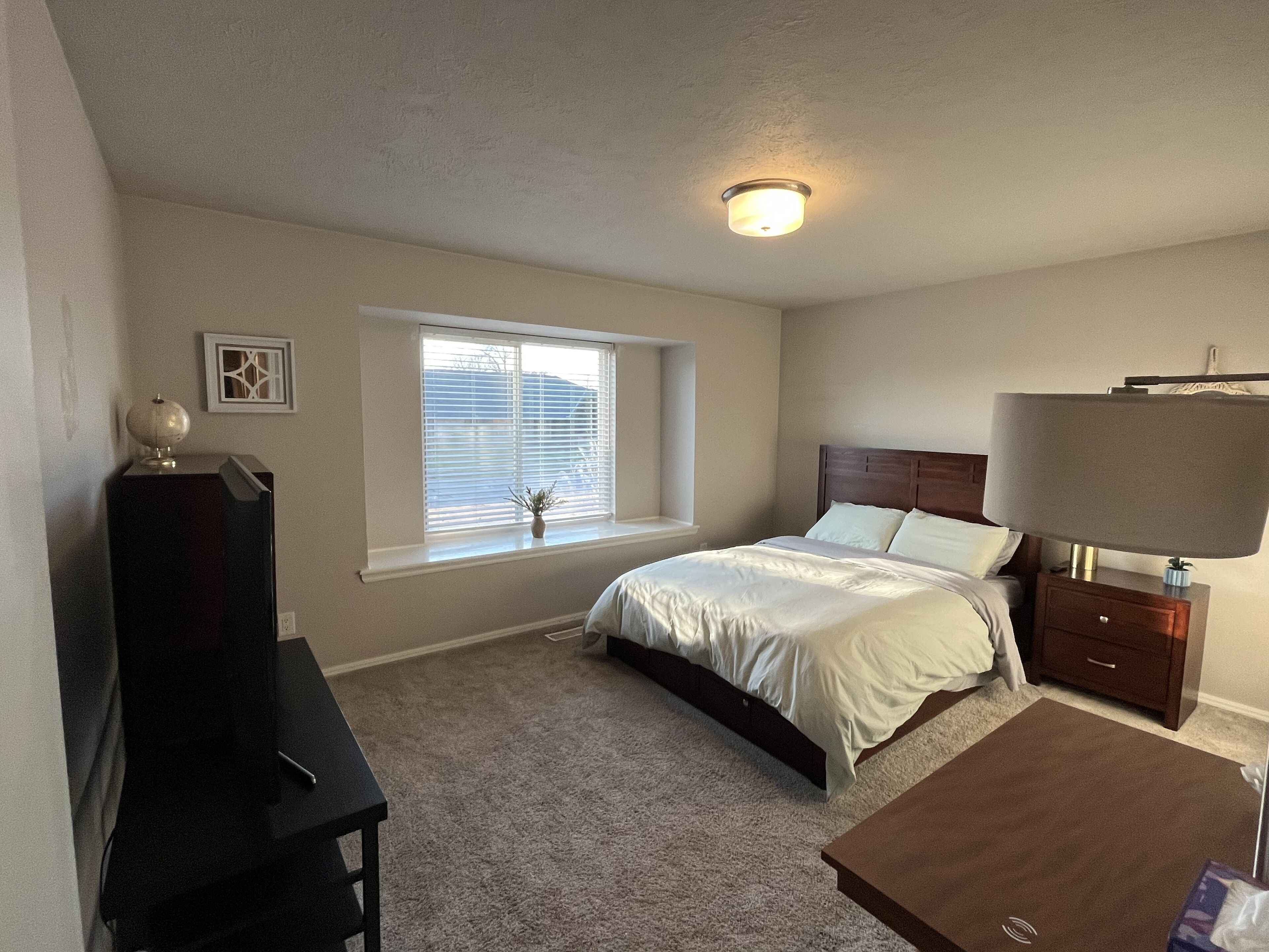 Une chambre à coucher avec un lit, une table de chevet, une lampe et une fenêtre avec des stores.