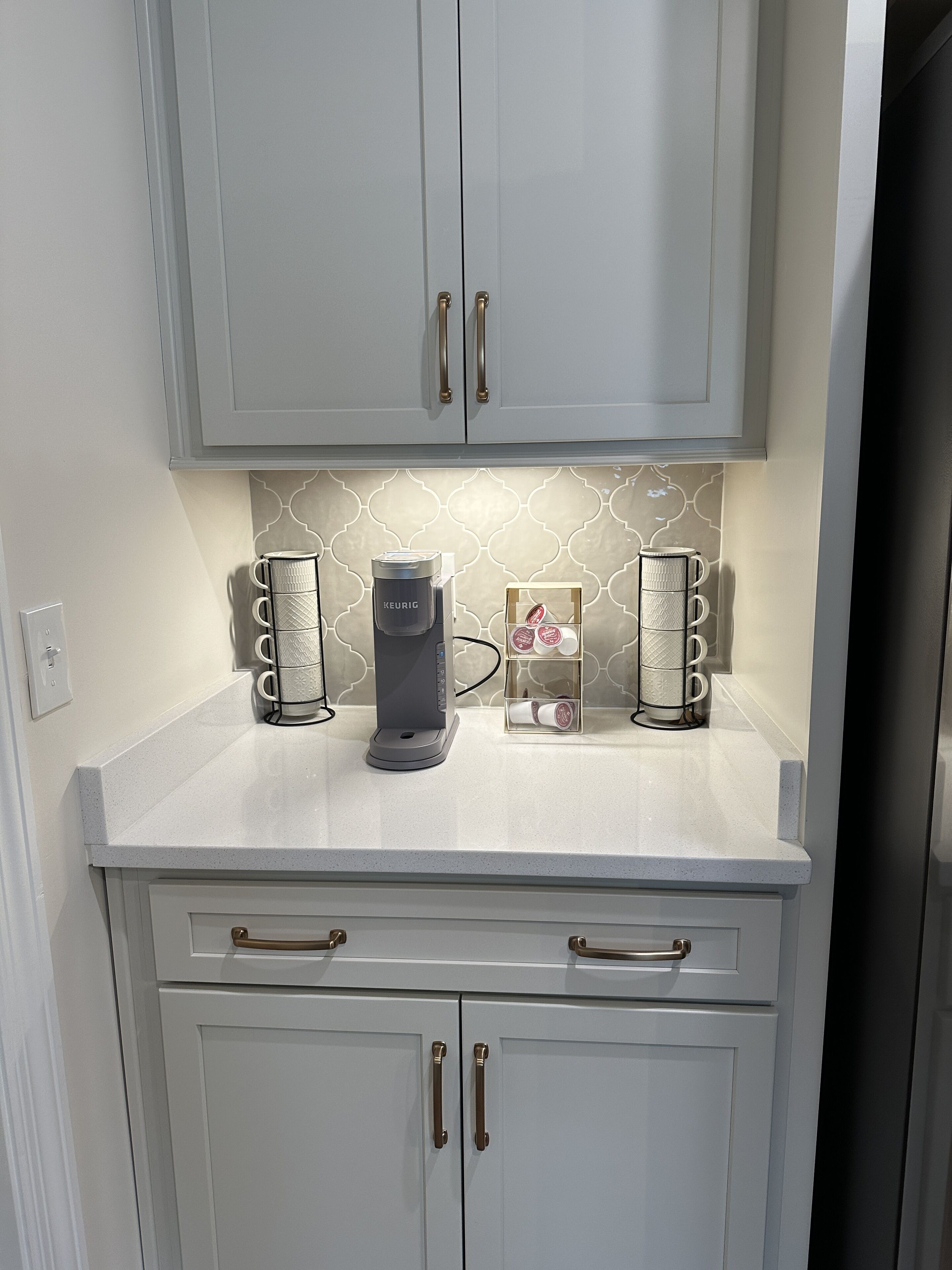 A kitchen with a coffee maker, two mugs, and a box of coffee pods on the counter.