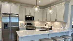 Una cocina moderna con electrodomésticos de acero inoxidable, una isla grande con taburetes de bar e iluminación colgante.