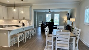 Una cocina moderna con armarios blancos, una isla central con taburetes y un comedor con mesa y sillas de madera.