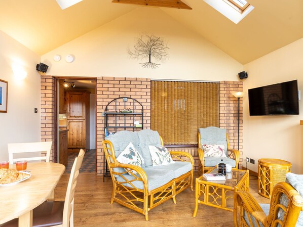 A cozy room with wicker furniture, a brick wall, a television, and a dining area with a table and chairs.