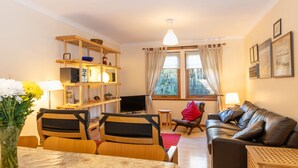 A cozy living room with a wooden bookshelf, a TV, a sofa, and a dining area with a table and chairs. - Culduthel by Interhome (Aviemore)