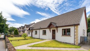 A row of white houses with brown roofs, a paved driveway, and a stone wall. - Culduthel by Interhome (Aviemore)