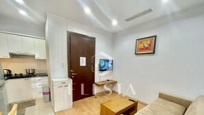 A compact living space with a kitchenette, a sofa, a coffee table, and a TV. - FLESTA Lê Thánh Tôn serviced apartment (Ho Chi Minh City)