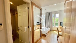 A spacious bedroom with a wooden floor, a large bed, a desk, and a window with curtains. - FLESTA Lê Thánh Tôn serviced apartment (Ho Chi Minh City)