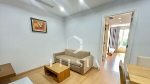 A modern living room with a sofa, a coffee table, and a dining table. There is a framed picture on the wall and a door leading to another room. - FLESTA Lê Thánh Tôn serviced apartment (Ho Chi Minh City)