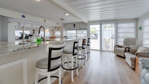 Una cocina amplia con armarios blancos, encimera de mármol y una zona de comedor con sillas y sofá blancos.