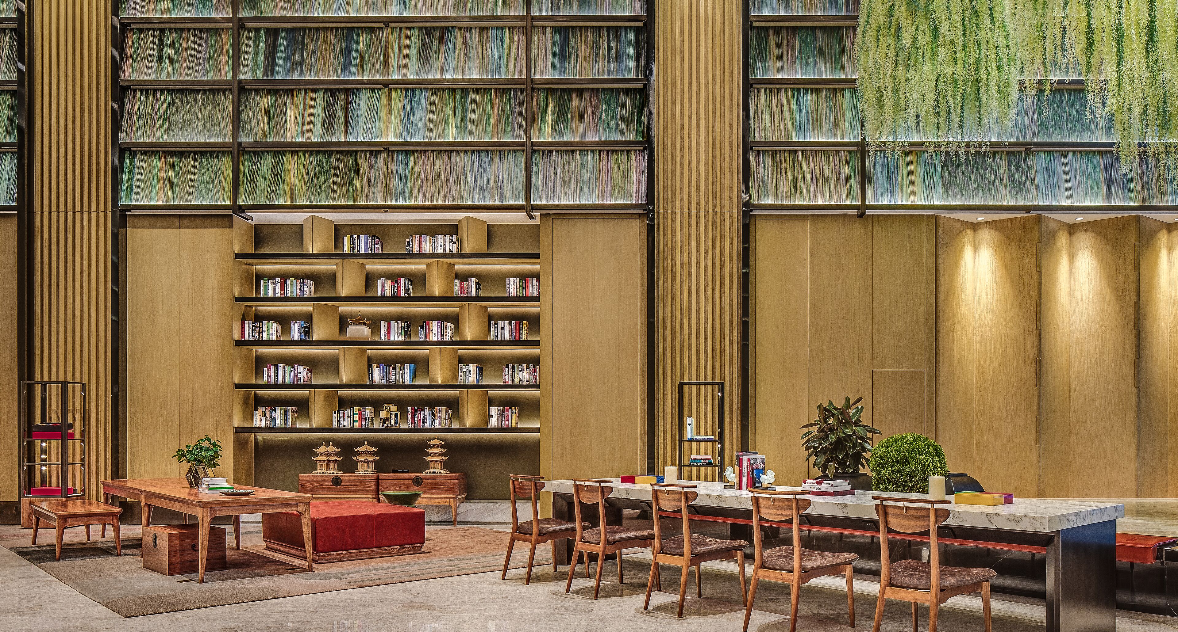 A library with bookshelves, a reading area with chairs and tables, and a decorative plant.
