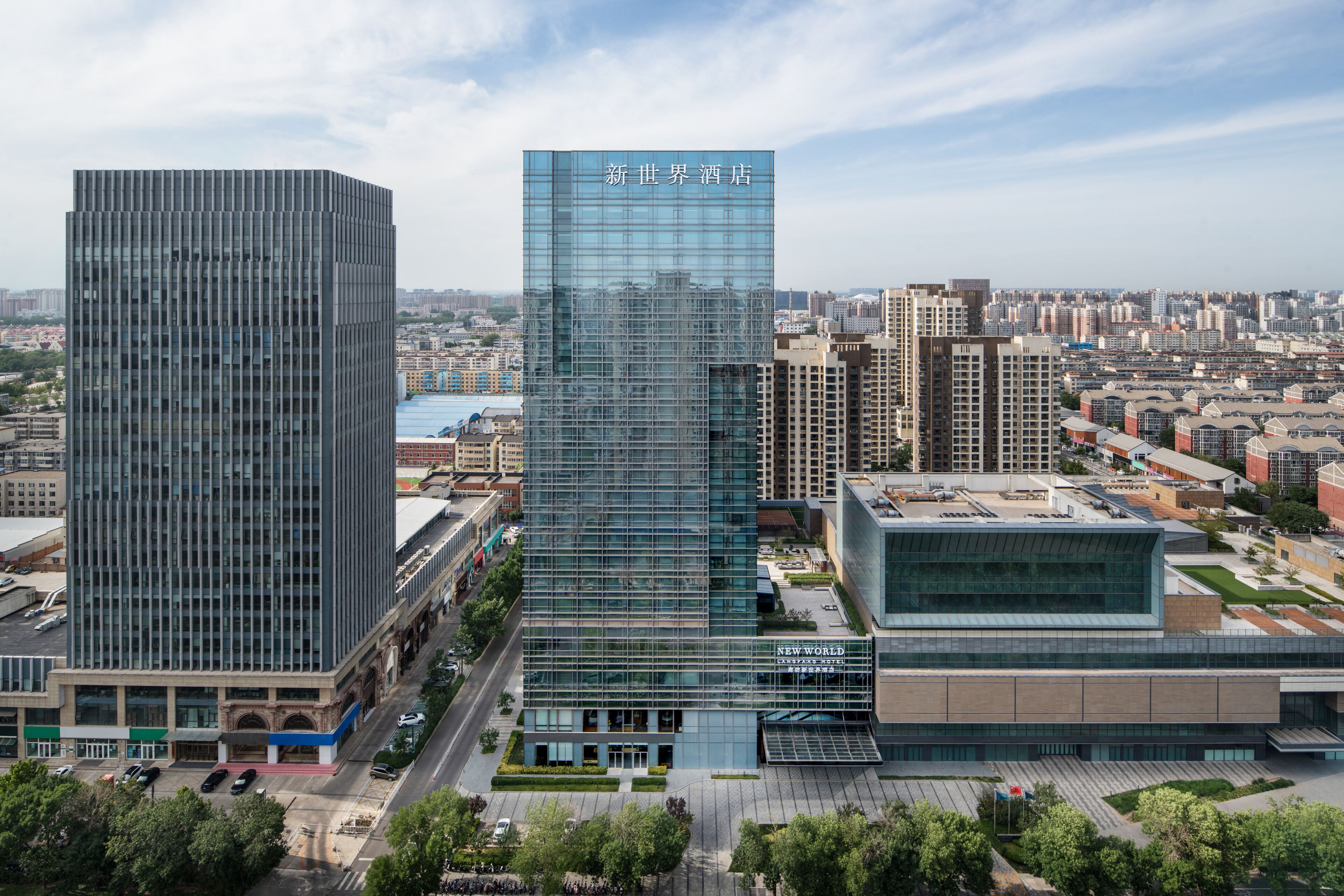 A modern hotel with a glass facade, surrounded by other buildings and a clear sky.