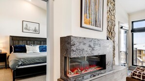 A modern bedroom with a large bed, a stone fireplace, and a view of the outside.
