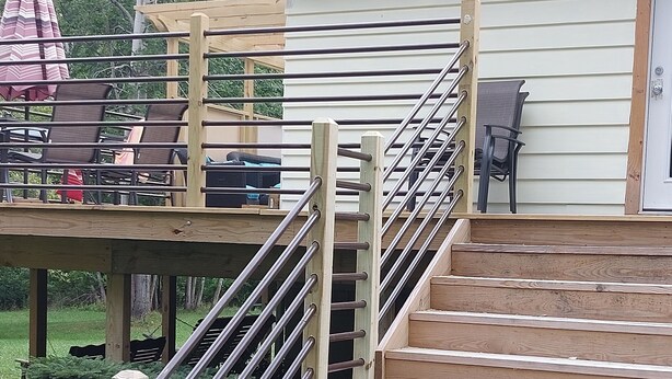 Eine Holztreppe führt zu einem Deck mit Metallgeländern, umgeben von viel Grün.