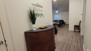 A hallway with a wooden cabinet, a decorative wall sign, and a seating area in the background.