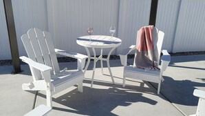 A white outdoor seating area with a round table and two chairs, each with a towel draped over one armrest.