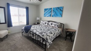 A bedroom with a bed, a chair, a small table, a lamp, and a window with curtains.