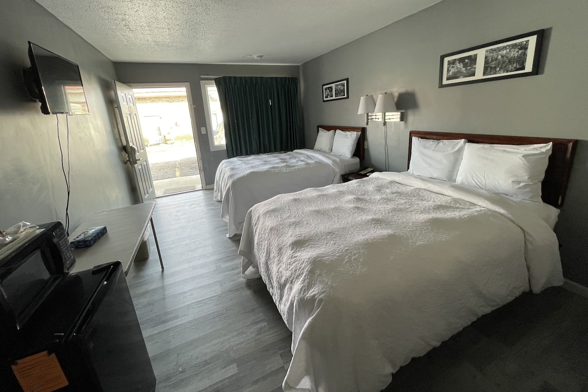 Quarto de hotel com duas camas, uma escrivaninha, uma televisão e vista para o exterior.
