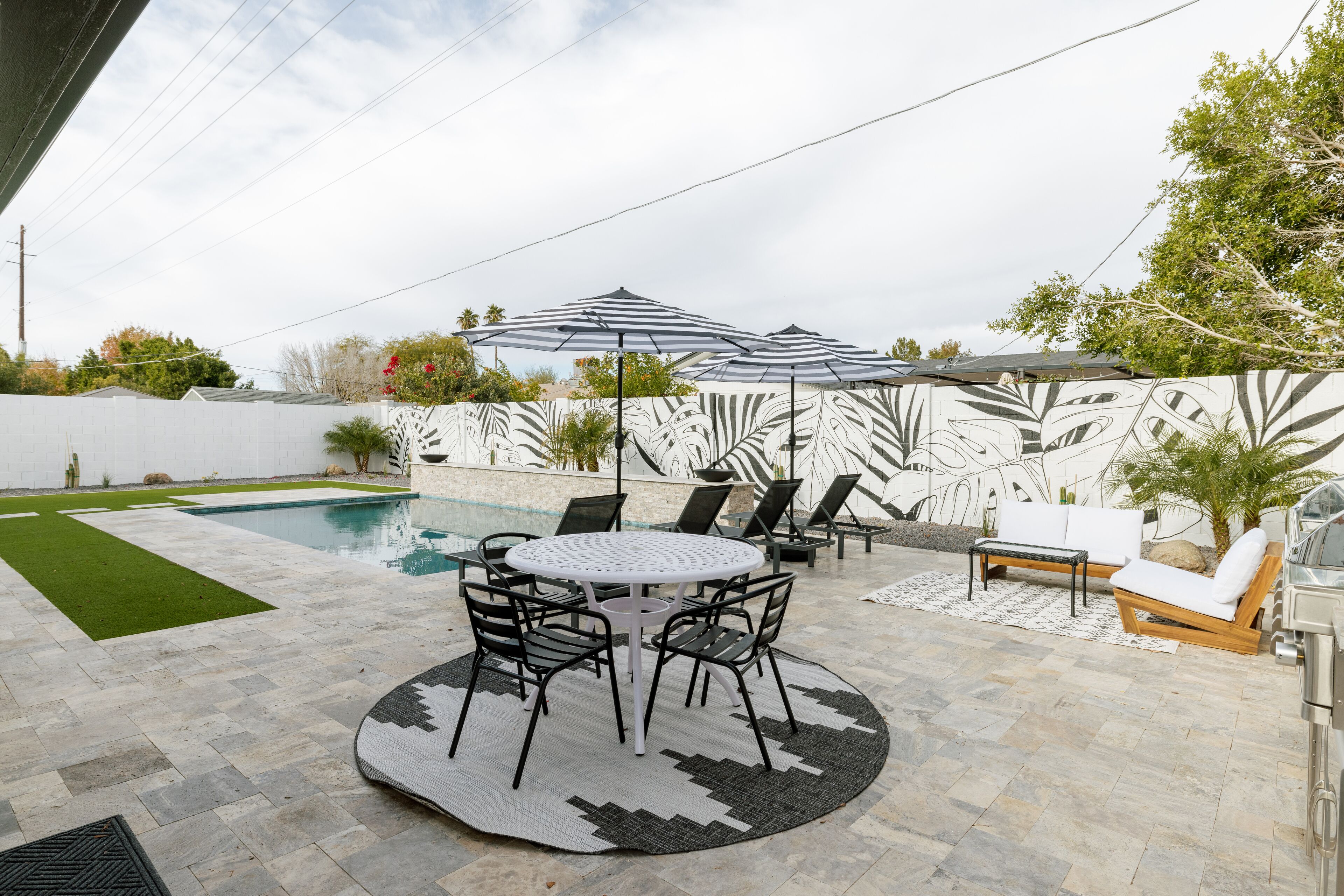 Eine Außenpatio mit Pool, einem runden Tisch mit Stühlen, Liegestühlen und Sonnenschirmen.