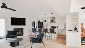 A modern living room with a fireplace, a dining area with chairs, and a kitchen with white cabinets and a black refrigerator. - Old Town Gem by Porter | Dog-Friendly Home w/Heated Pool and Arcade Games (Scottsdale)