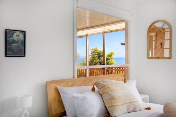 Een slaapkamer met een bed, een raam met uitzicht op zee, een houten hoofdeinde en een ingelijst kunstwerk aan de muur.
