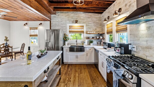 A kitchen with a central island, wooden ceiling beams, a stainless steel refrigerator, and a large stove.