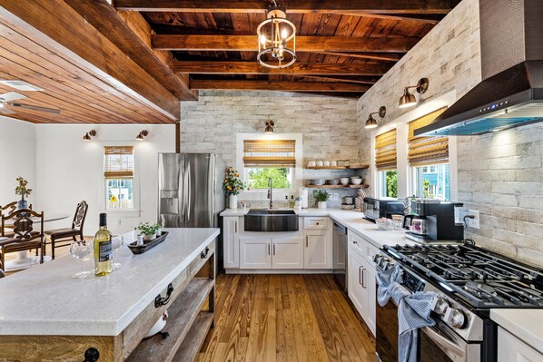 A kitchen with a central island, wooden ceiling beams, a stainless steel refrigerator, and a large stove.