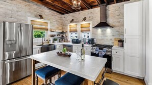 A kitchen with a central island, stainless steel appliances, and a brick wall.