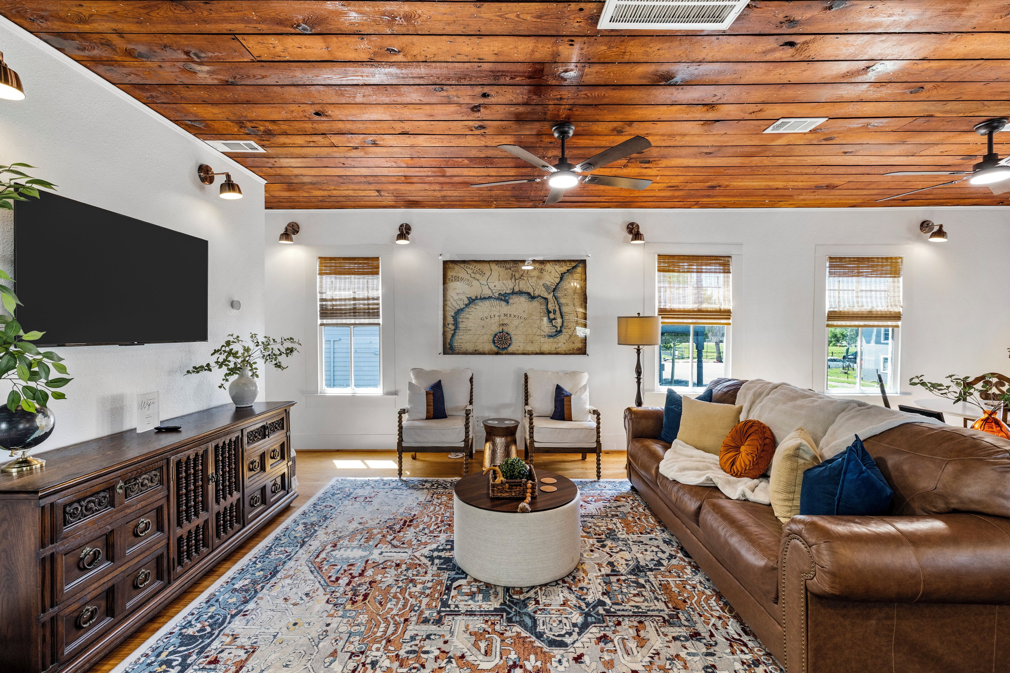 Un salon avec un plafond en bois, un grand téléviseur à écran plat, un canapé en cuir marron, un tapis à motifs et une carte accrochée au mur.