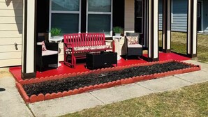 A two-story house with a covered front porch, large windows, and a red outdoor seating area. - Cozy 5 bedroom/ 9 beds, 3 full baths with game room (Huntsville)