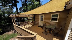 Eine Holzterrasse mit einer Pergola, einem Tisch mit Stühlen und einer zur Hausführung.