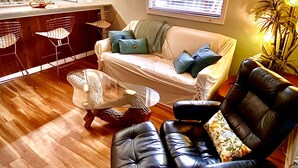 A cozy living room with a sofa, two armchairs, a coffee table, and a dining area with a kitchen in the background.