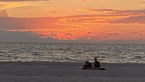 A beach with two people sitting on the sand, facing the ocean.