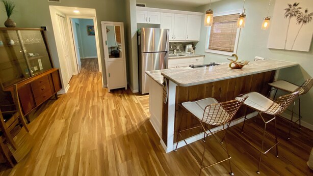 A modern kitchen with wooden flooring, a central island with bar stools, stainless steel appliances, and pendant lighting.