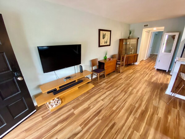 Una sala de estar con televisor de pantalla plana, muebles de madera y un comedor con sillas y un aparador.