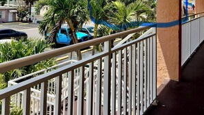 A balcony with a view of a street, palm trees, and a building in the background.