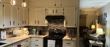 A kitchen with white cabinets, a black stove, and a ceiling fan.