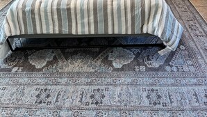 Un lit avec une couvre-lit à rayures, deux oreillers, une tête de lit, une table de chevet avec une lampe et un tapis à motifs.