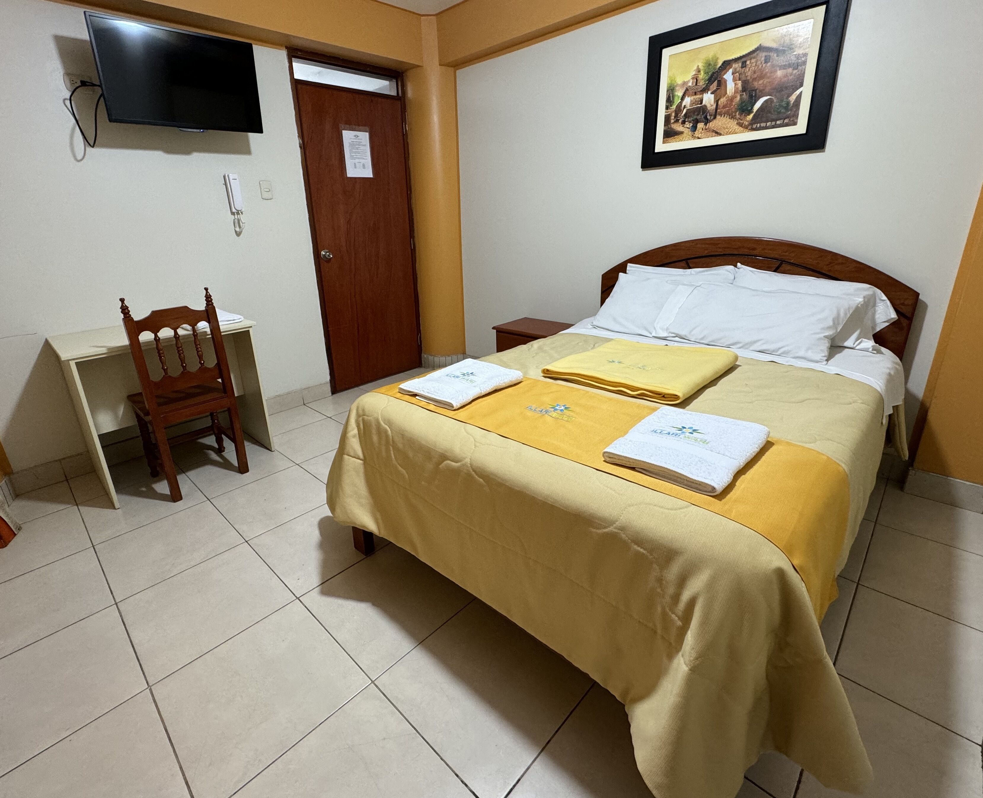 Una habitación de hotel con una cama, un escritorio, una silla, un televisor y un cuadro en la pared.