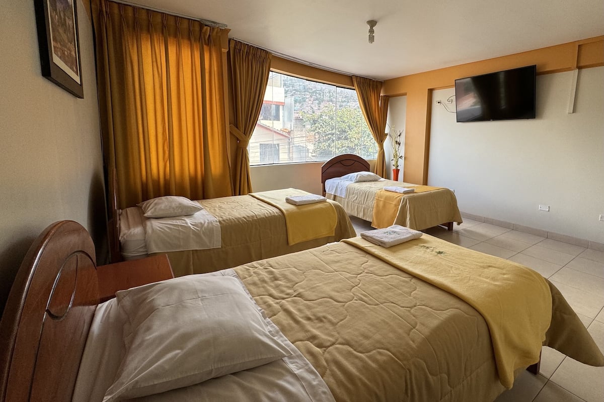 Habitación de hotel con dos camas, un televisor en la pared y un ventanal con cortinas.