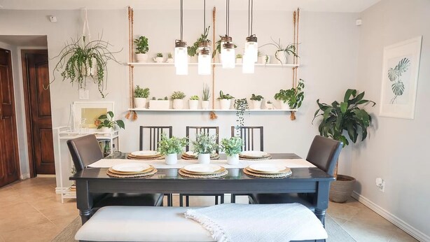 Een eetgedeelte met een zwarte tafel voor vier personen, omringd door stoelen. Daarboven hangen planten en hanglampen.