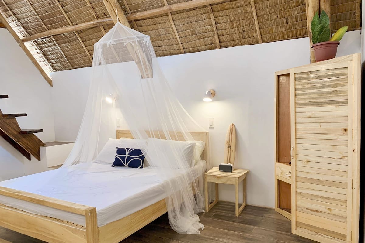 A bedroom with a wooden bed, a nightstand, a bedside table, a wardrobe, a potted plant, and a staircase.